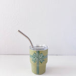 Green cup with a patterned design and metal straw on a white background