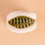 White textured pouch with a gold zipper on a beige background