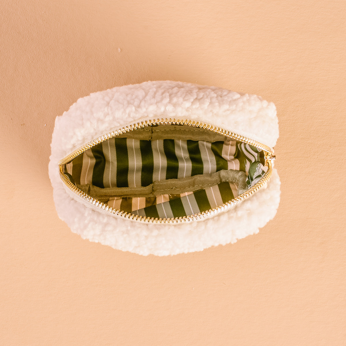 White textured pouch with a gold zipper on a beige background