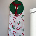 Decorative towel with Christmas patterns hanging on a hook against a white wall.