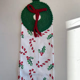 Decorative towel with Christmas patterns hanging on a hook against a white wall.