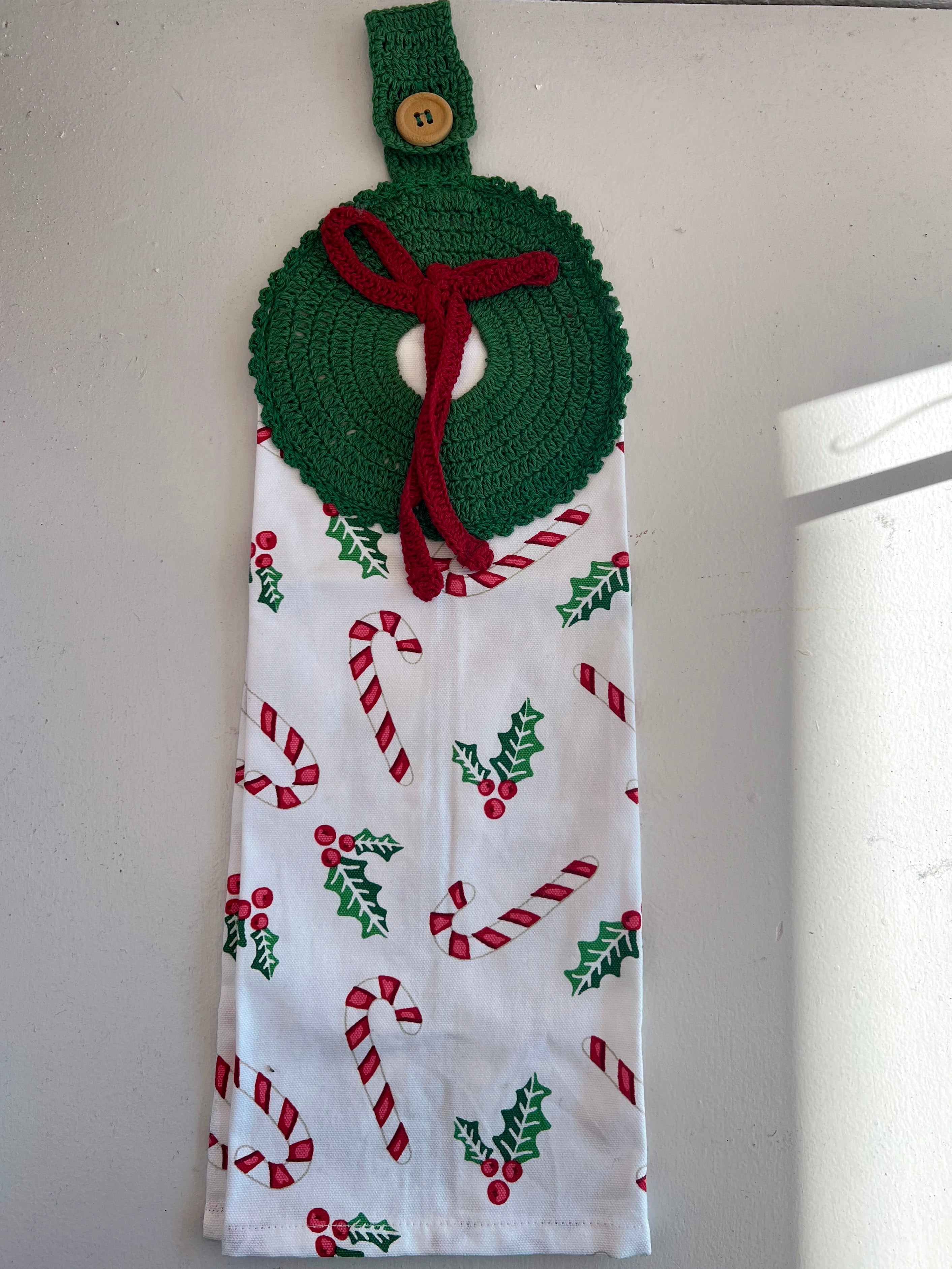 Decorative towel with Christmas patterns hanging on a hook against a white wall.