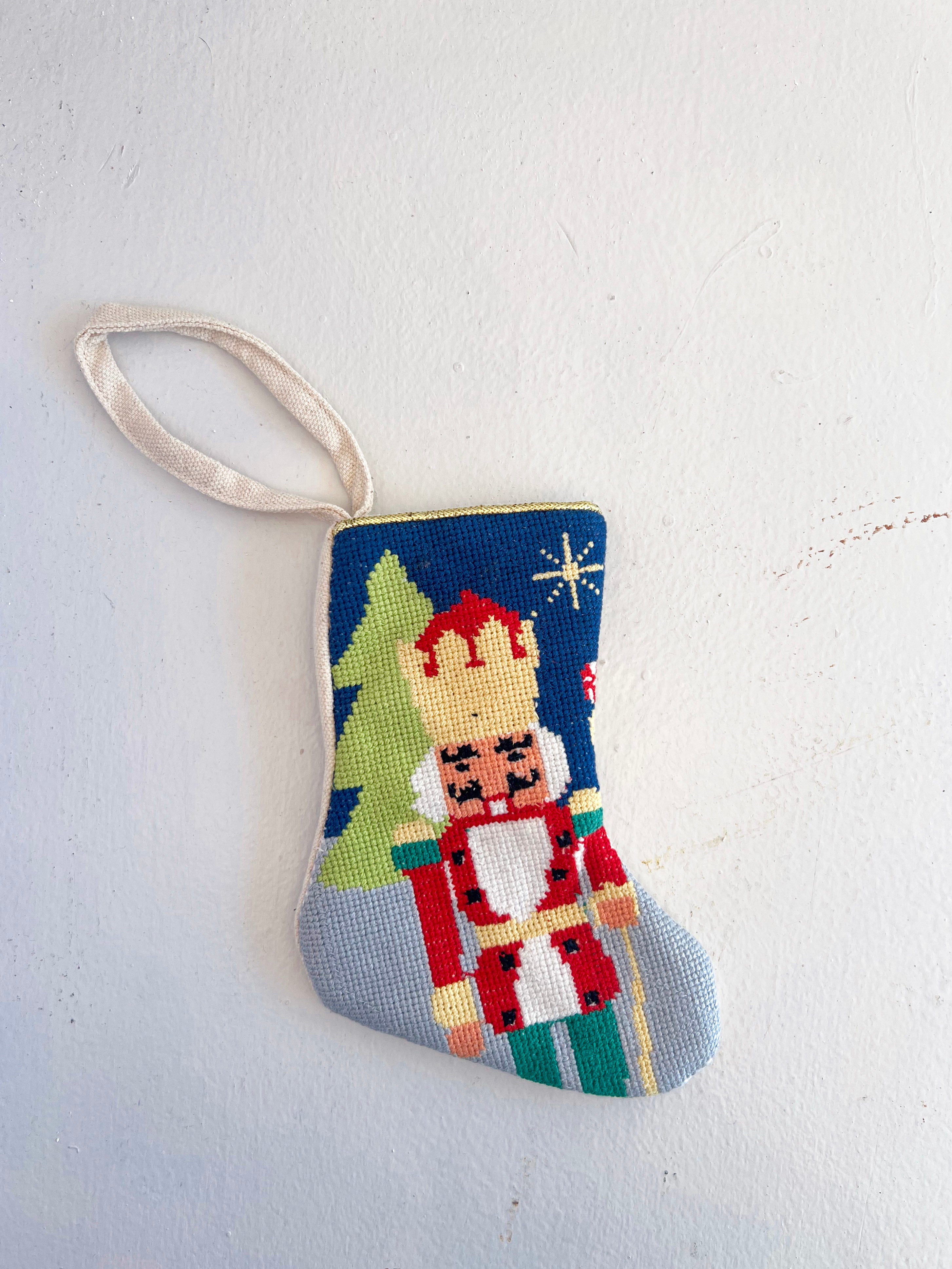 Decorative needlepoint ornament with a nutcracker design on a white background