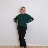 Person wearing a green sweater with polka dot sleeves against a white wall.