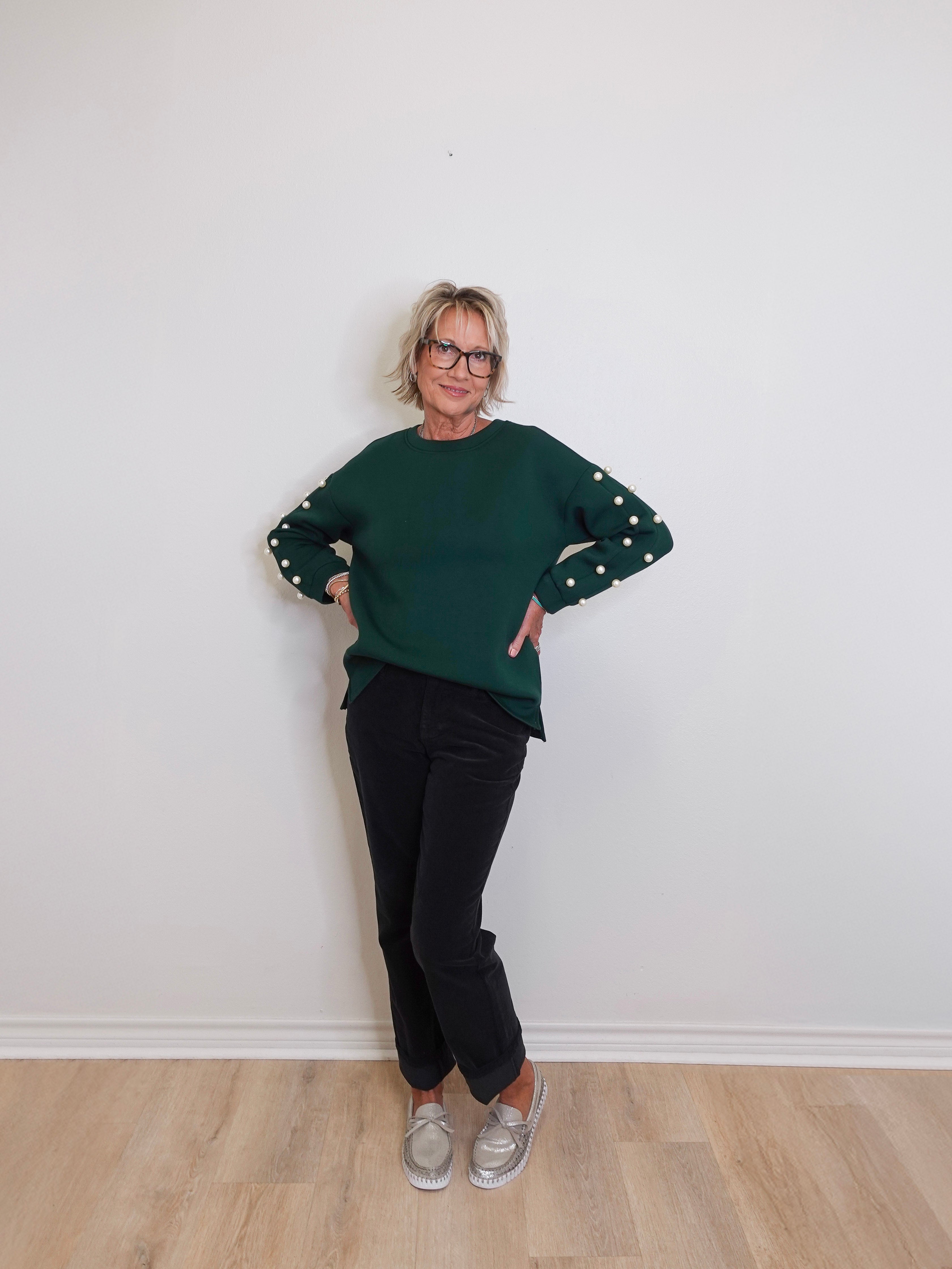 Person wearing a green sweater with polka dot sleeves against a white wall.