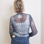 Person wearing a patterned top and jeans against a plain background