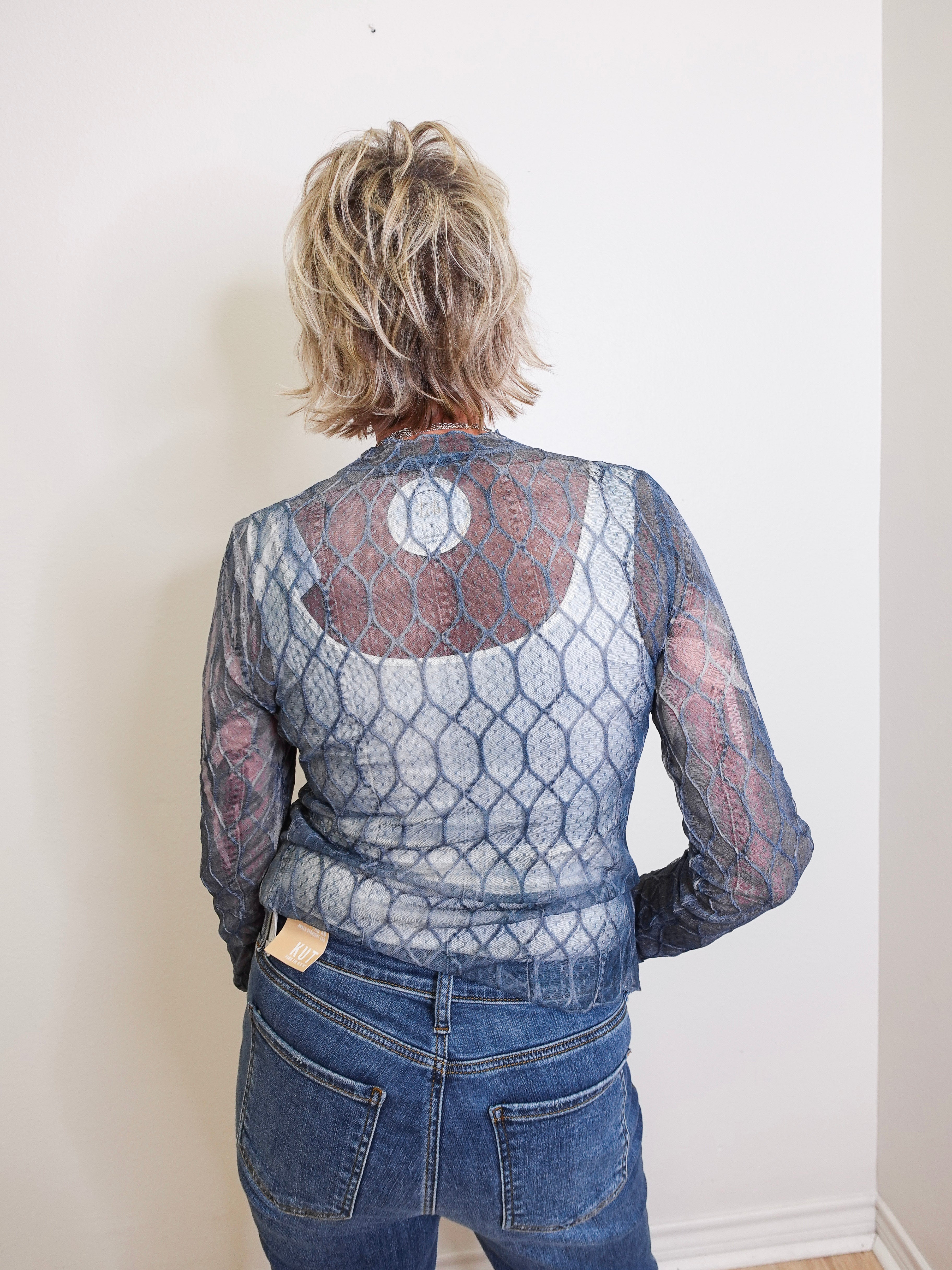 Person wearing a patterned top and jeans against a plain background