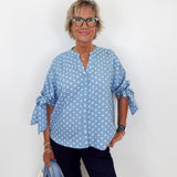 Woman wearing a blue polka dot shirt and black pants against a white background