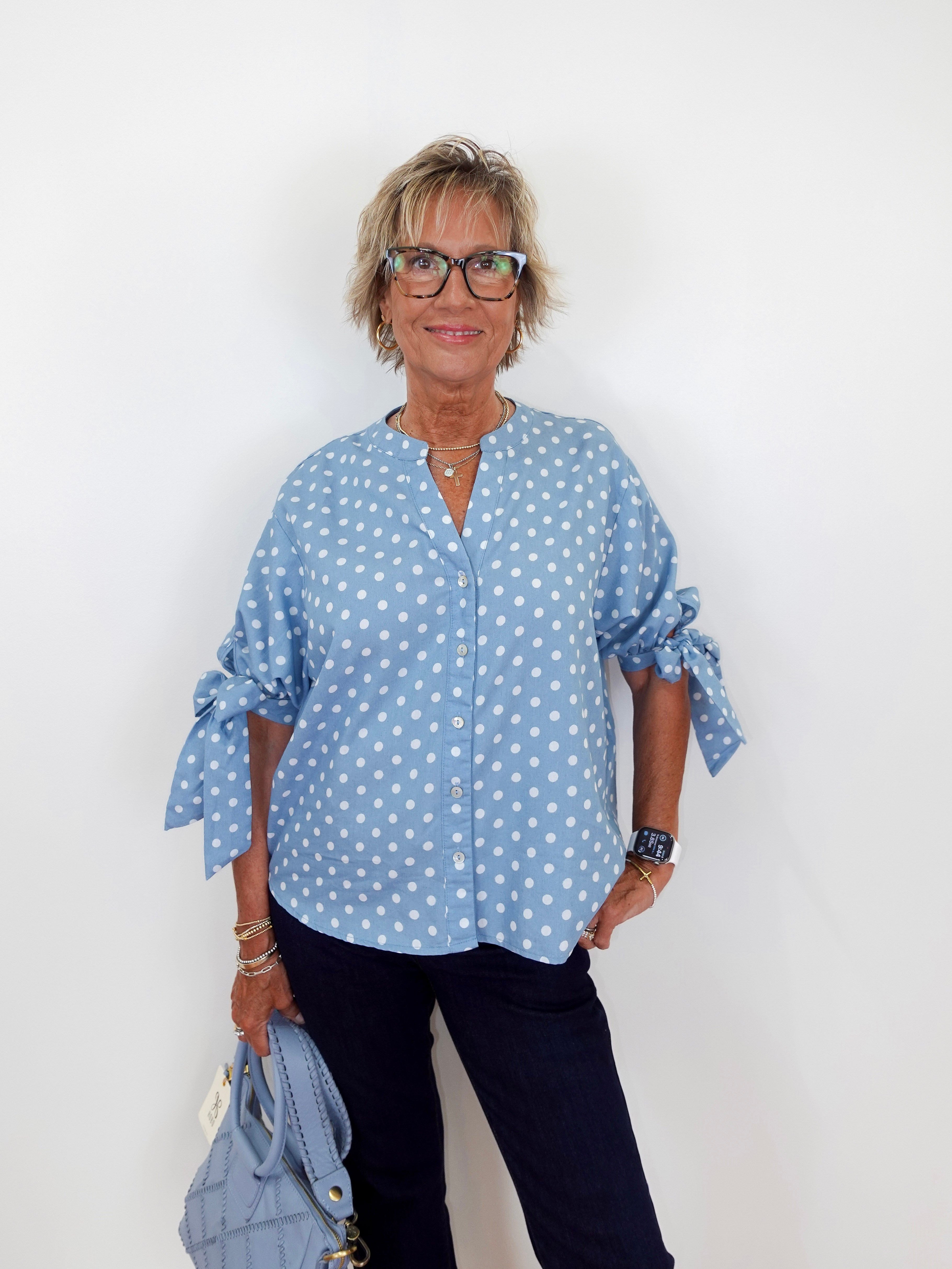 Woman wearing a blue polka dot shirt and black pants against a white background