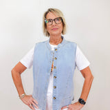 Woman wearing a light blue denim vest over a white shirt against a plain background