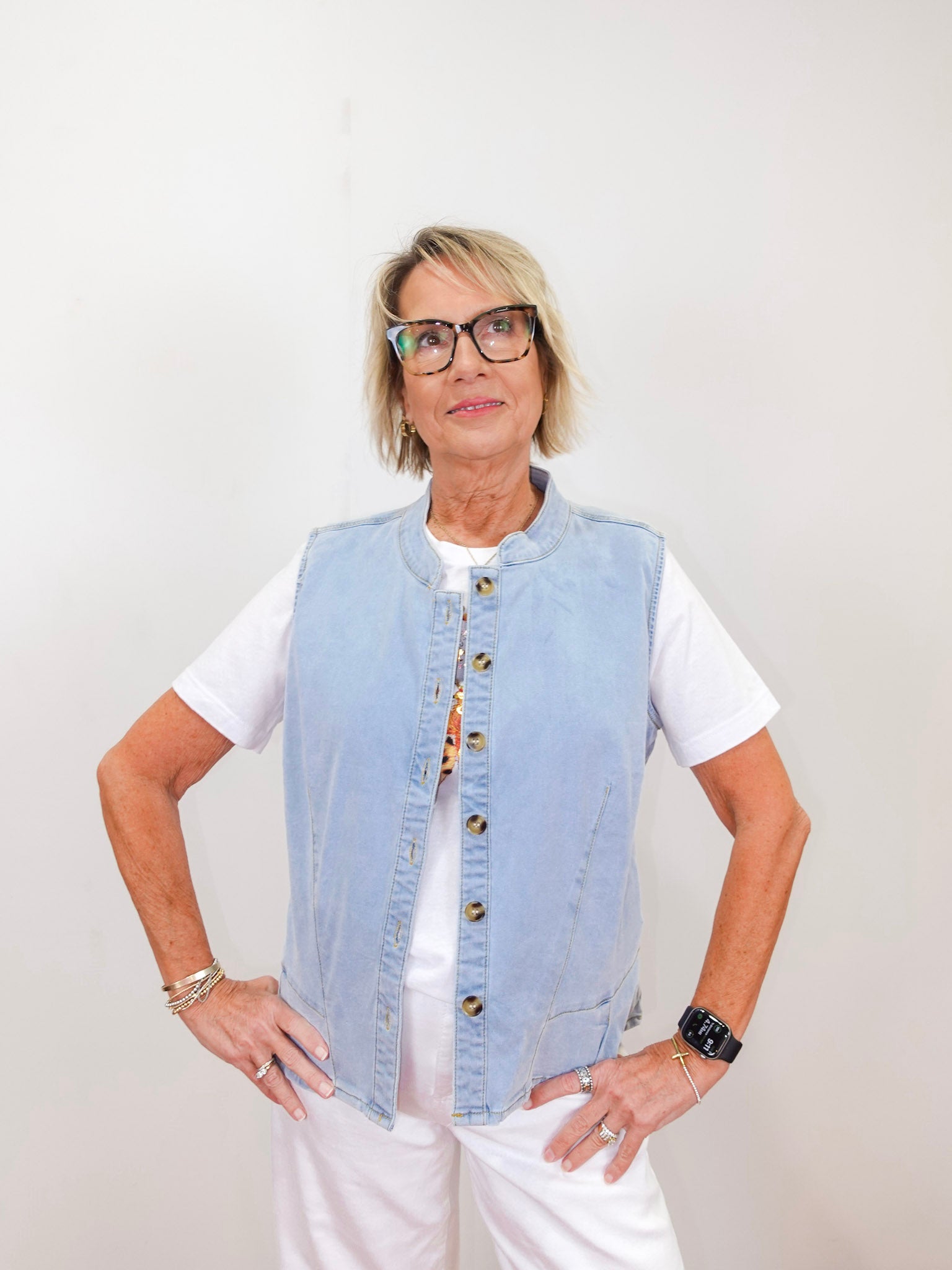 Woman wearing a light blue denim vest over a white shirt against a plain background