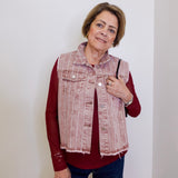 Woman wearing a red shirt and denim vest against a white wall