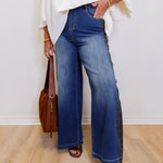Person wearing blue jeans and a white top, standing against a plain background