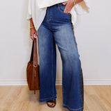 Person wearing blue jeans and a white top, standing against a plain background