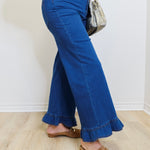 Person wearing blue flared jeans and brown loafers against a white wall.
