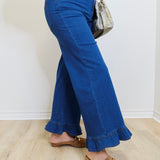 Person wearing blue flared jeans and brown loafers against a white wall.