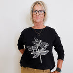 Person wearing a black sweater with dragonfly design on a white background