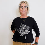 Person wearing a black sweater with dragonfly design on a white background