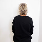 Person wearing a black sweater and beige pants against a white wall