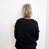 Person wearing a black sweater and beige pants against a white wall