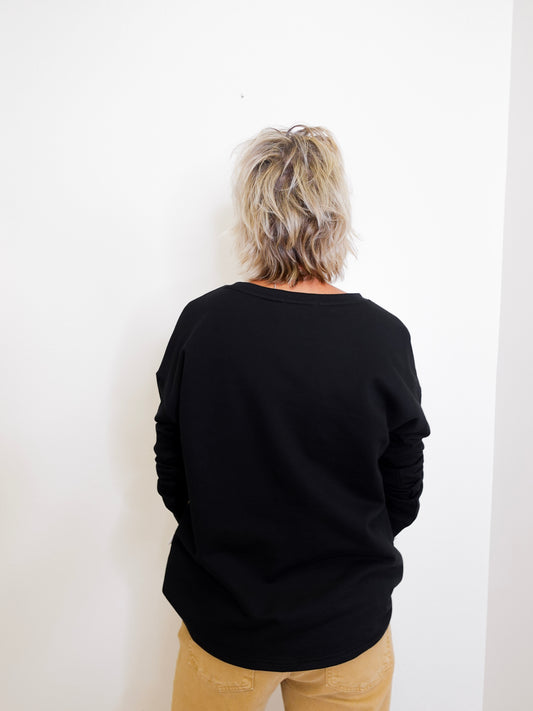 Person wearing a black sweater and beige pants against a white wall