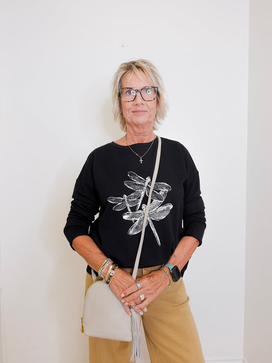 Woman wearing a black sweater with dragonfly design, holding a white bag against a white background