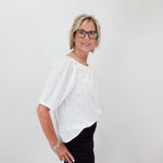 Woman wearing a white blouse with a subtle pattern and black shorts against a plain background