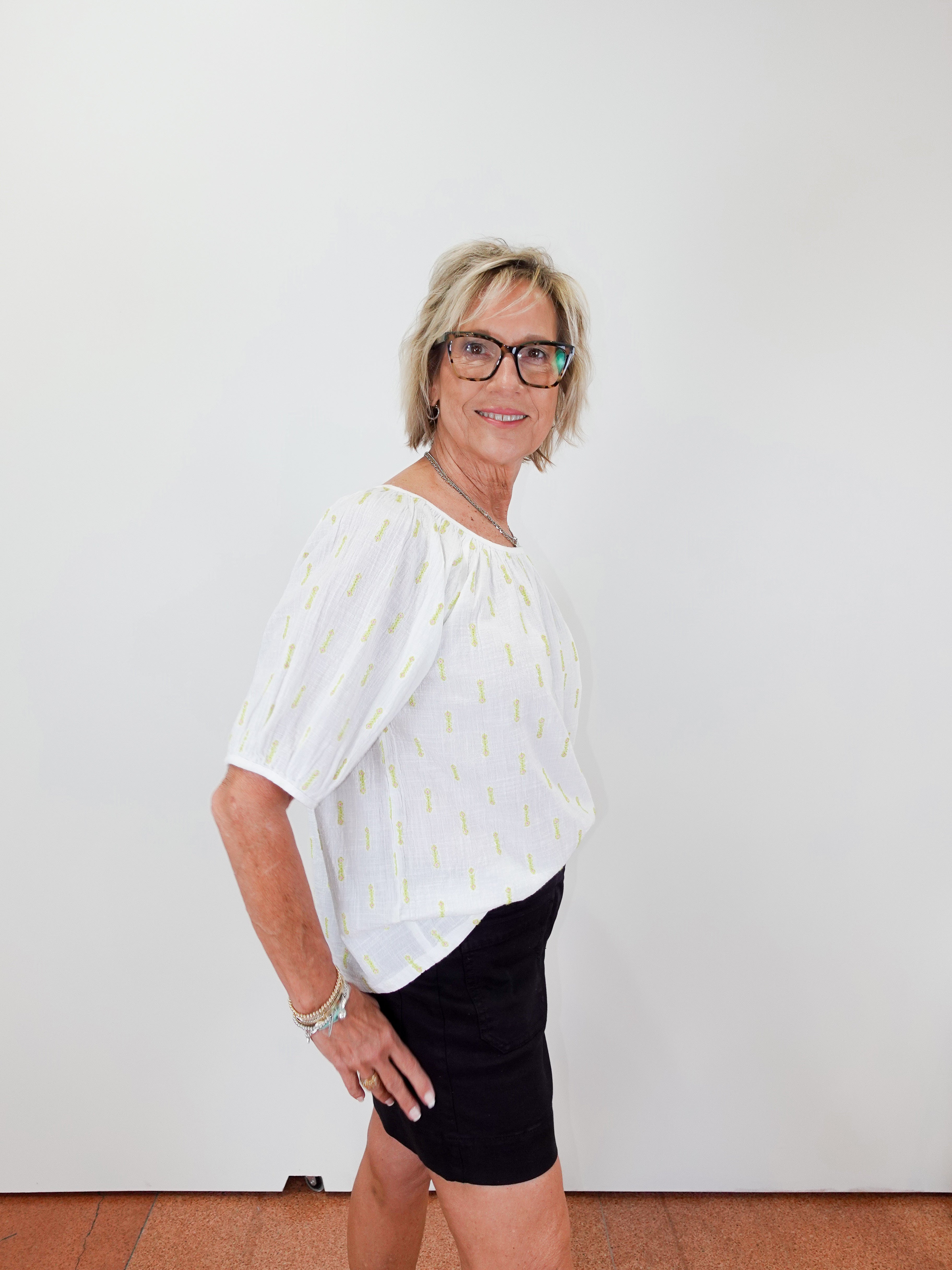 Woman wearing a white blouse with a subtle pattern and black shorts against a plain background