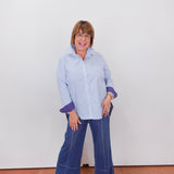 Woman wearing a blue and white striped shirt and blue jeans standing against a white wall.