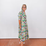 Woman wearing a colorful dress with a pattern of butterflies against a white wall.