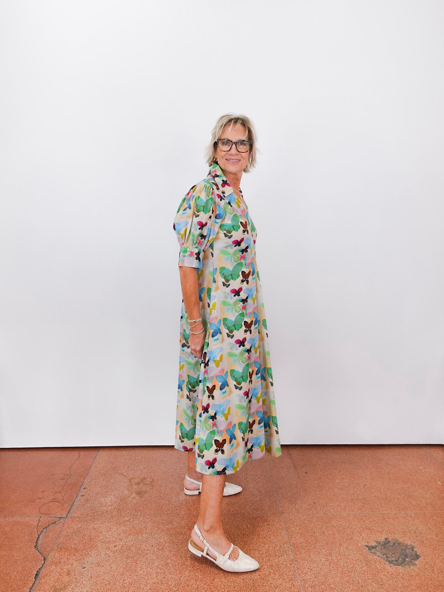 Woman wearing a colorful dress with a pattern of butterflies against a white wall.
