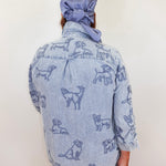 Person wearing a denim jacket with dog patterns and a matching headscarf against a white background