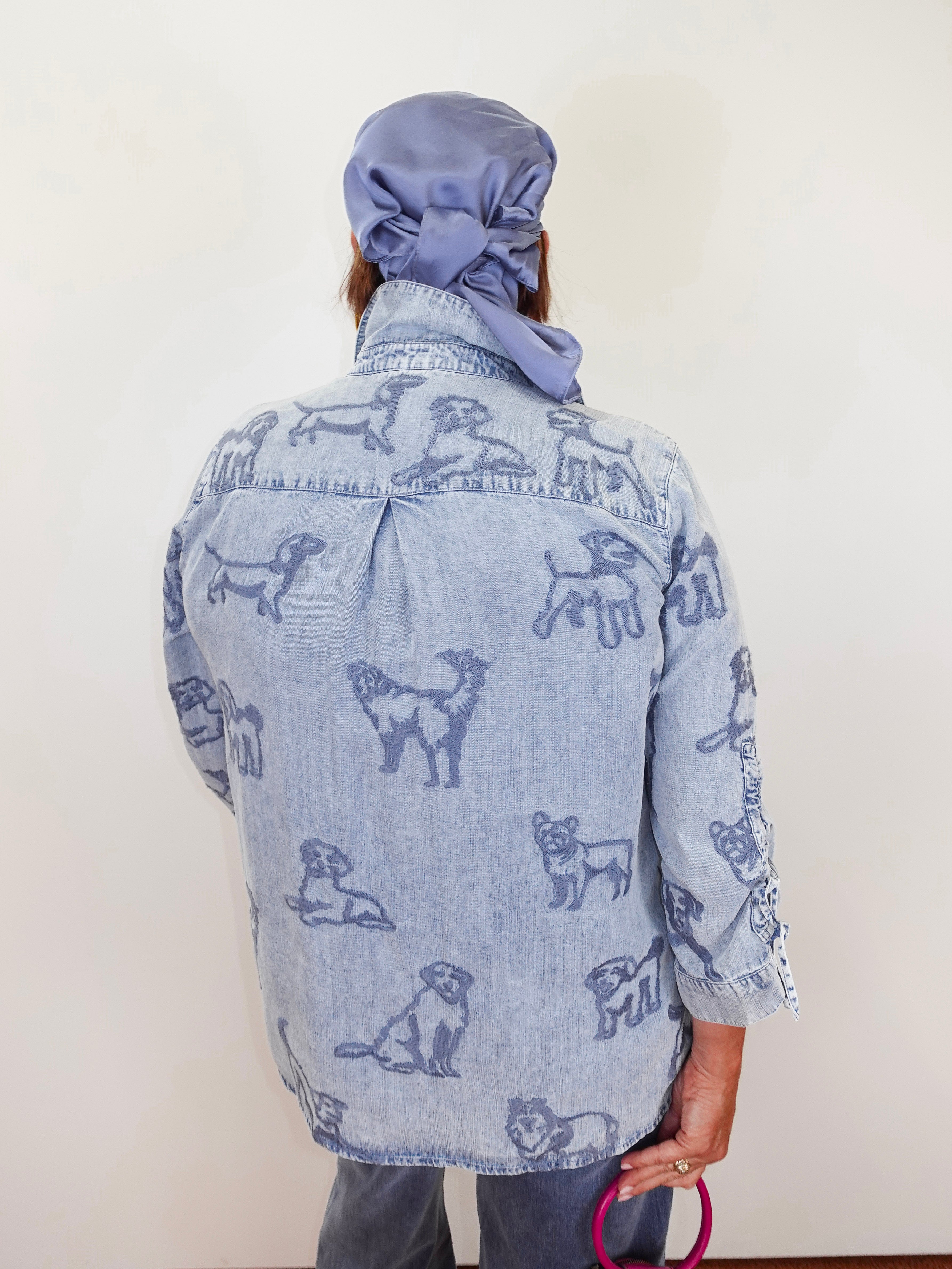 Person wearing a denim jacket with dog patterns and a matching headscarf against a white background