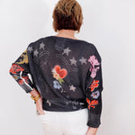 Person wearing a black sweater with colorful floral and star patterns on a white background
