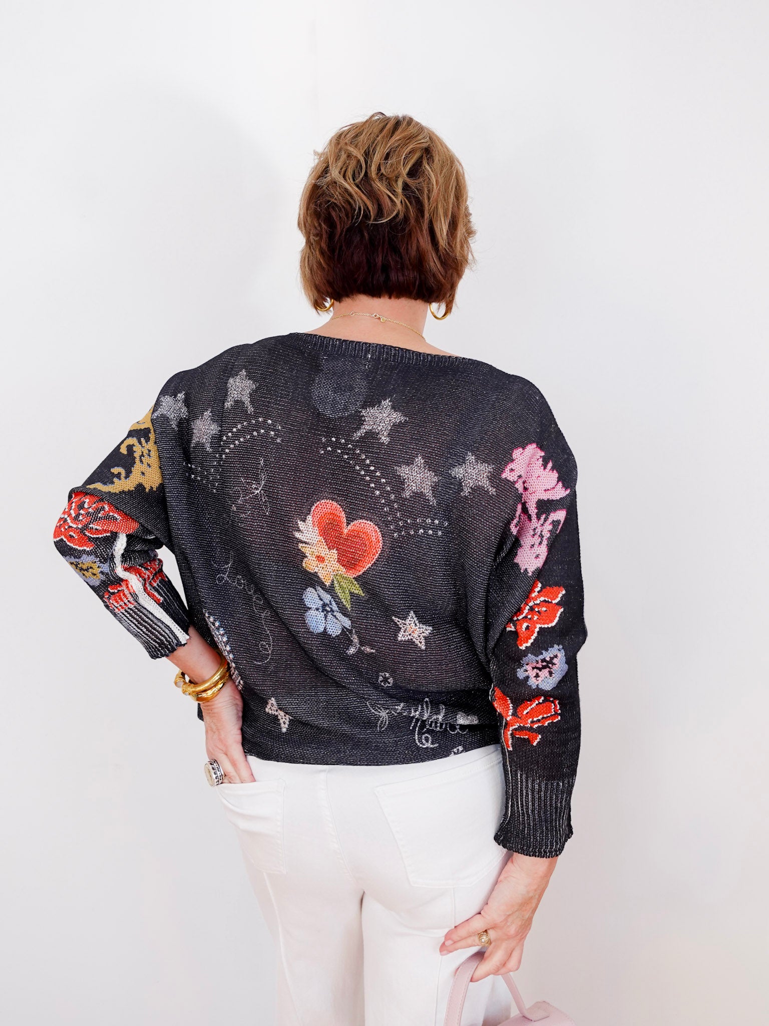 Person wearing a black sweater with colorful floral and star patterns on a white background