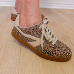 Leopard print sneakers with brown soles worn indoors on a wooden floor.