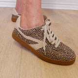 Leopard print sneakers with brown soles worn indoors on a wooden floor.