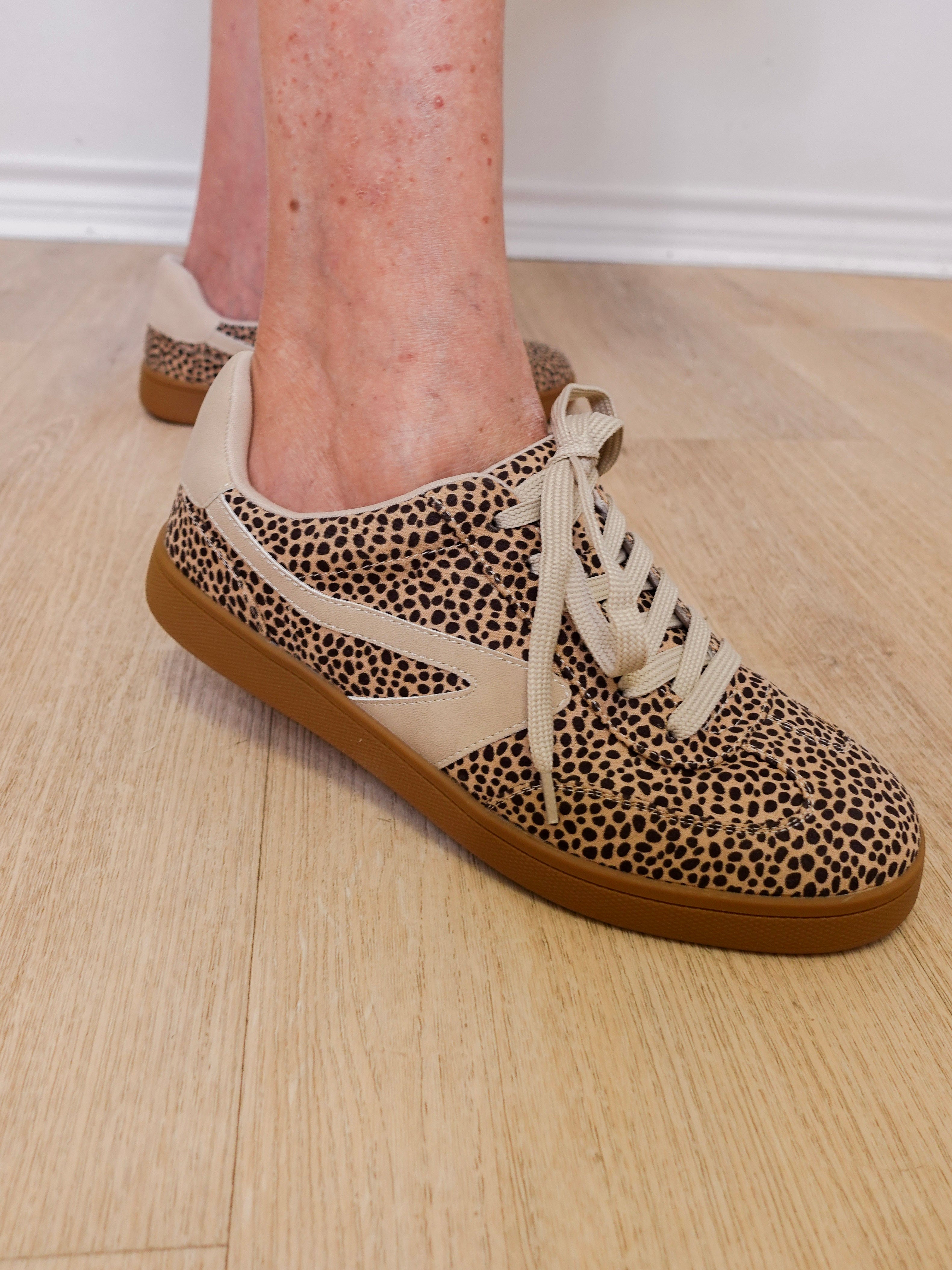 Leopard print sneakers with brown soles worn indoors on a wooden floor.