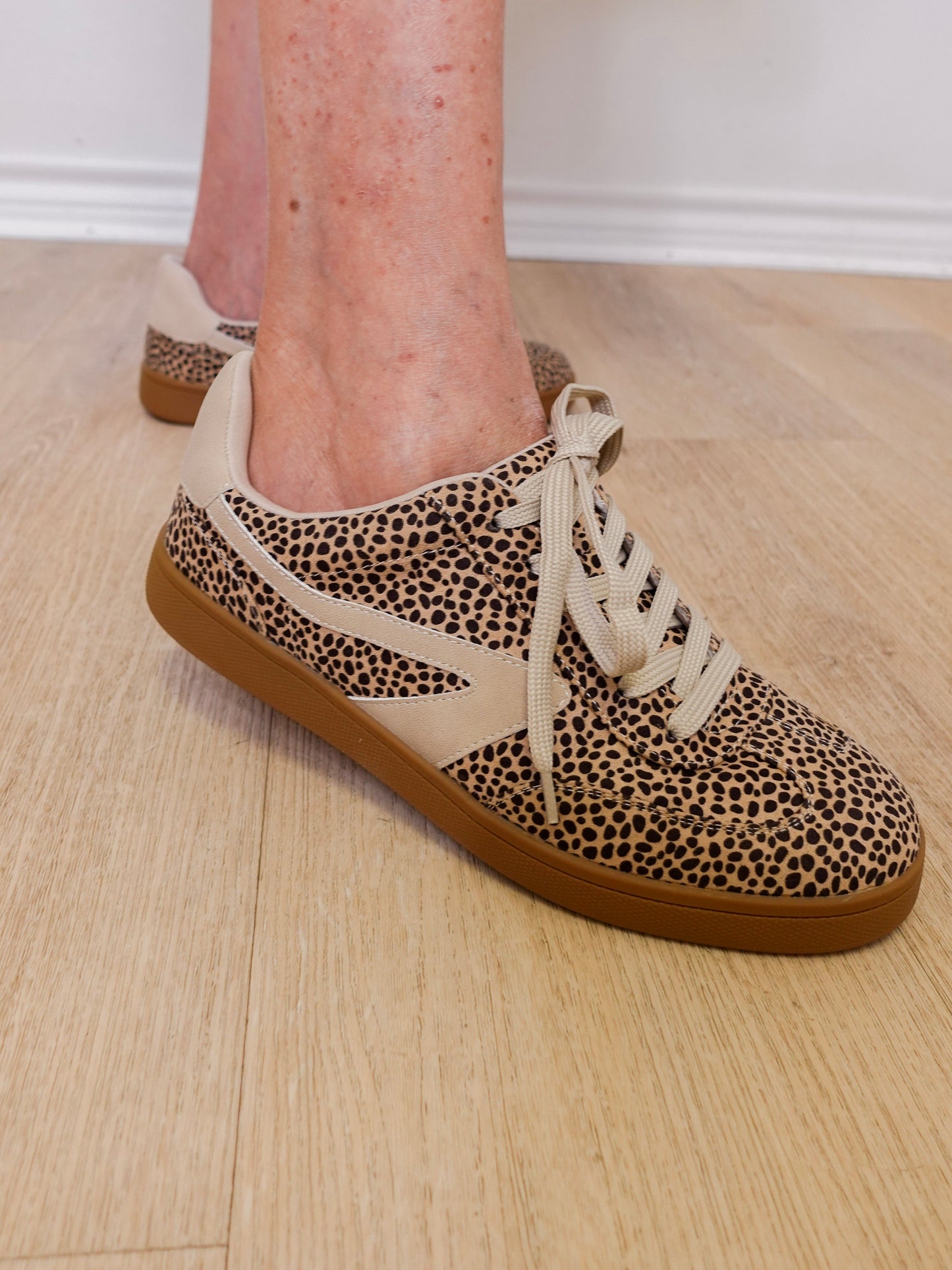 Leopard print sneakers with brown soles worn indoors on a wooden floor.