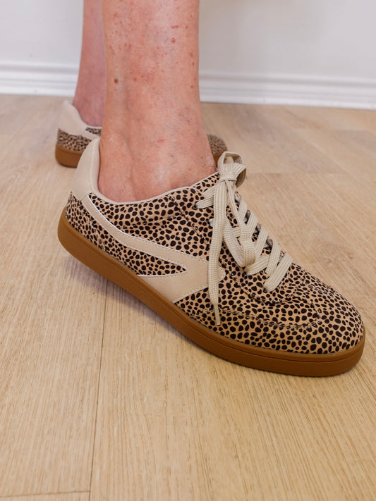 Leopard print sneakers with brown soles worn indoors on a wooden floor.