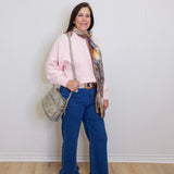 Woman wearing a pink blouse, blue jeans, and brown shoes against a white wall.