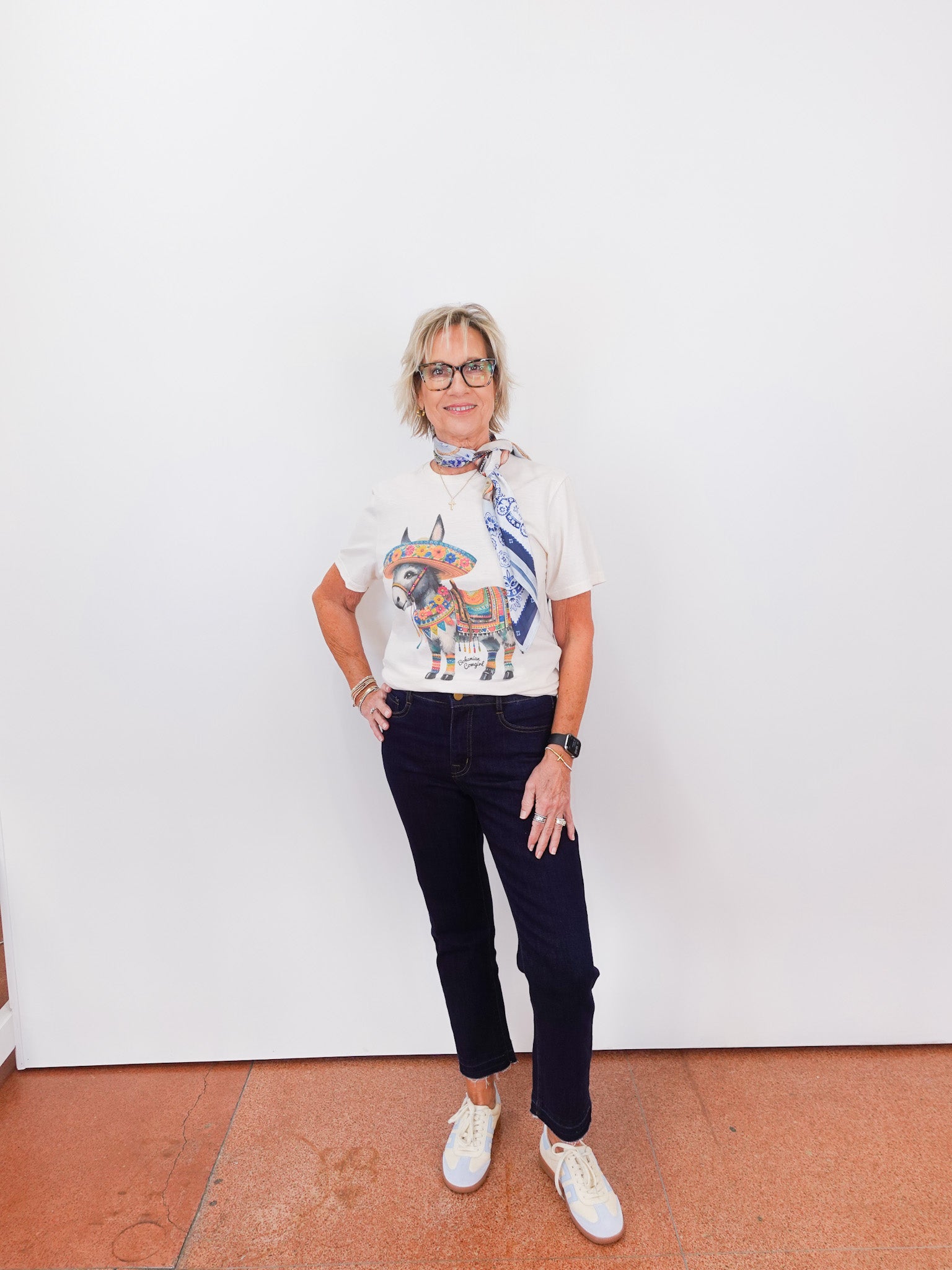 Person wearing a white t-shirt with a graphic design and dark jeans against a white wall.