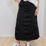 Person wearing a black ruched skirt and white sneakers on a plain background