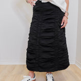 Person wearing a black ruched skirt and white sneakers on a plain background