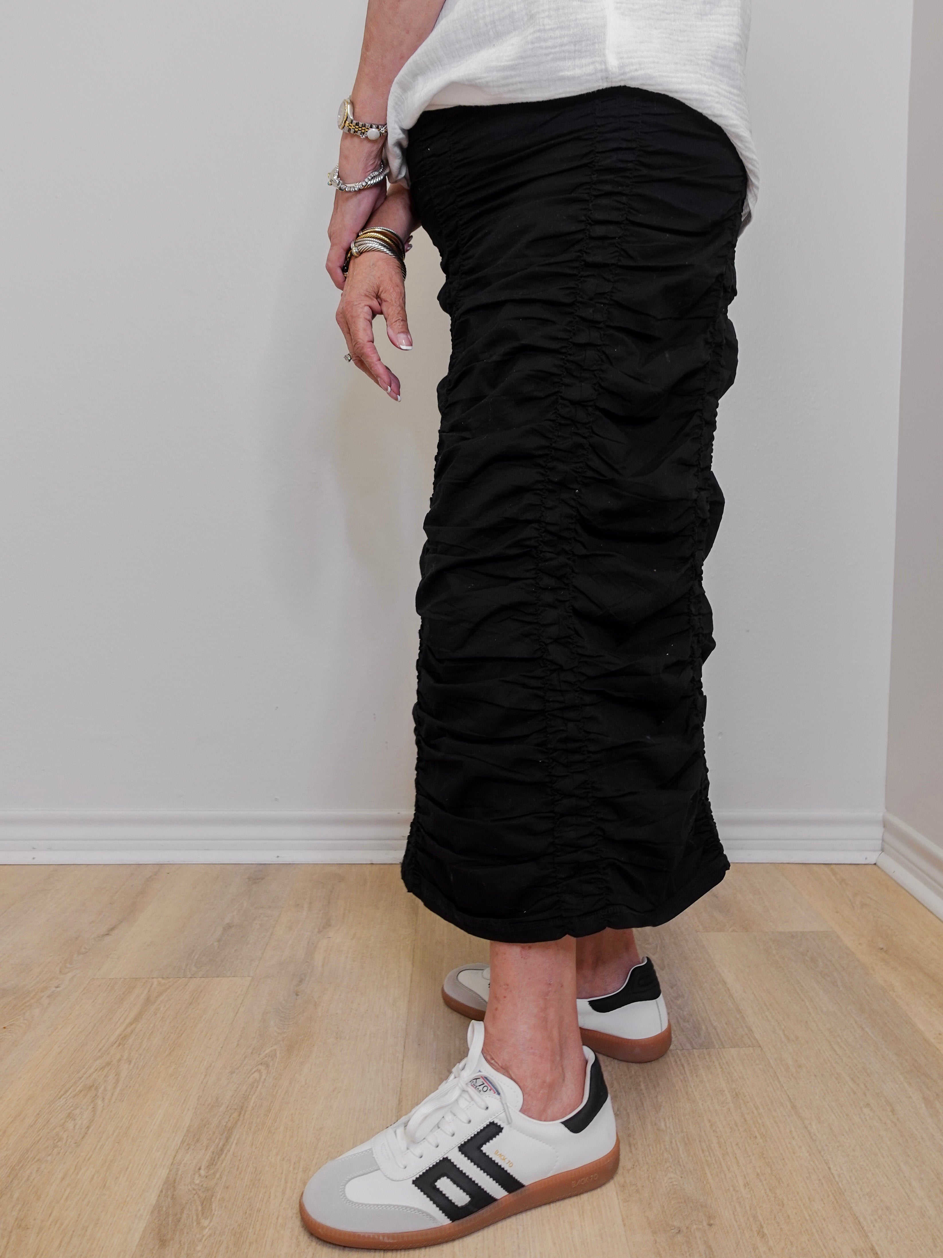 Person wearing black ruched pants and white sneakers on a plain background