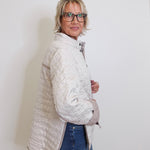 Woman wearing a light gray quilted jacket and blue jeans against a white background