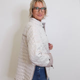 Woman wearing a light gray quilted jacket and blue jeans against a white background