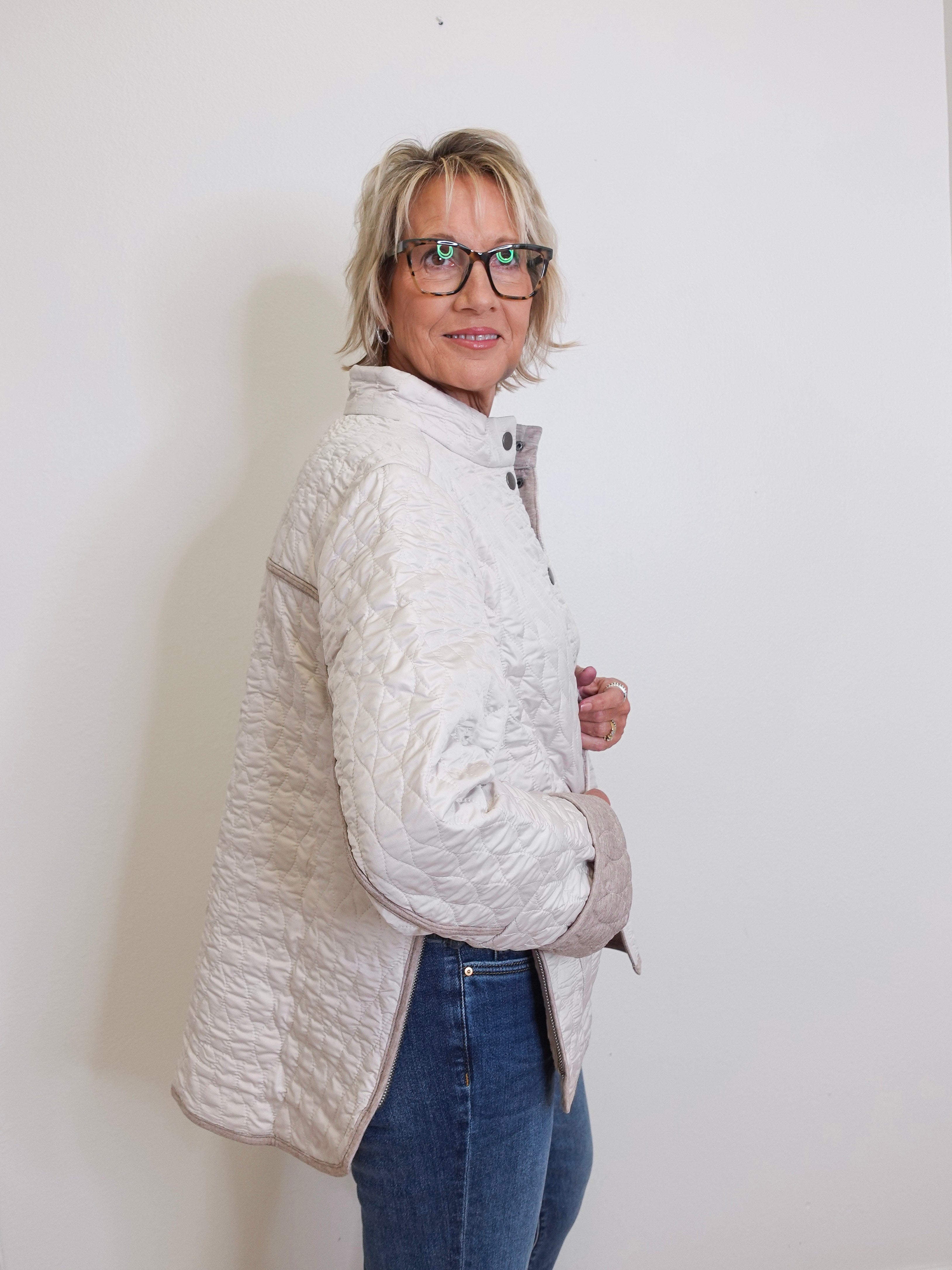 Woman wearing a light gray quilted jacket and blue jeans against a white background