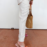 Person wearing white pants and colorful sandals on a brown floor.