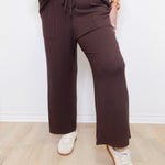 Person wearing brown pants and white sneakers against a white wall.